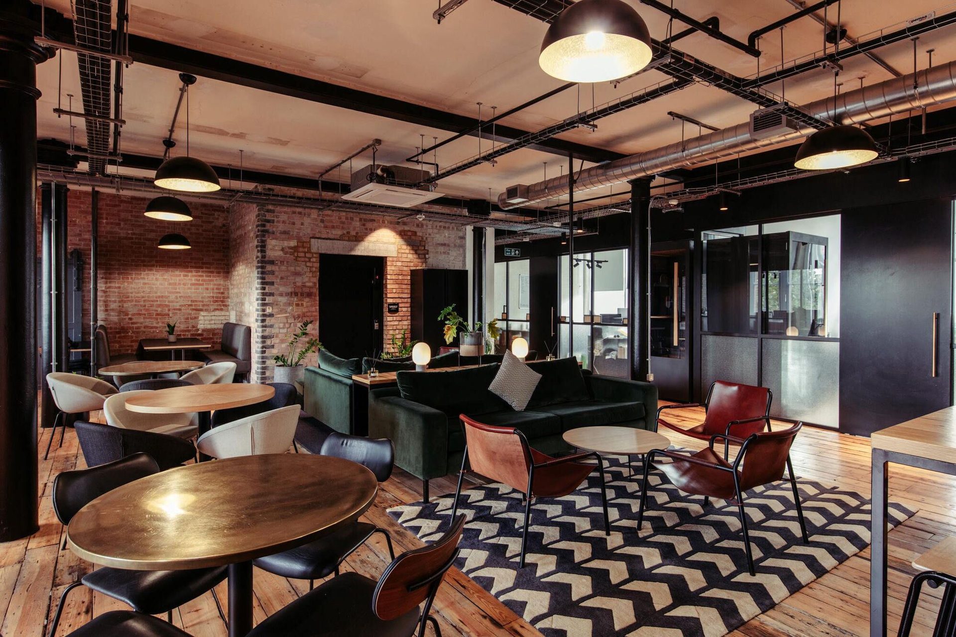 A brick-walled lounge at The Ministry with a green sofa, pendant lighting and leather armchairs
