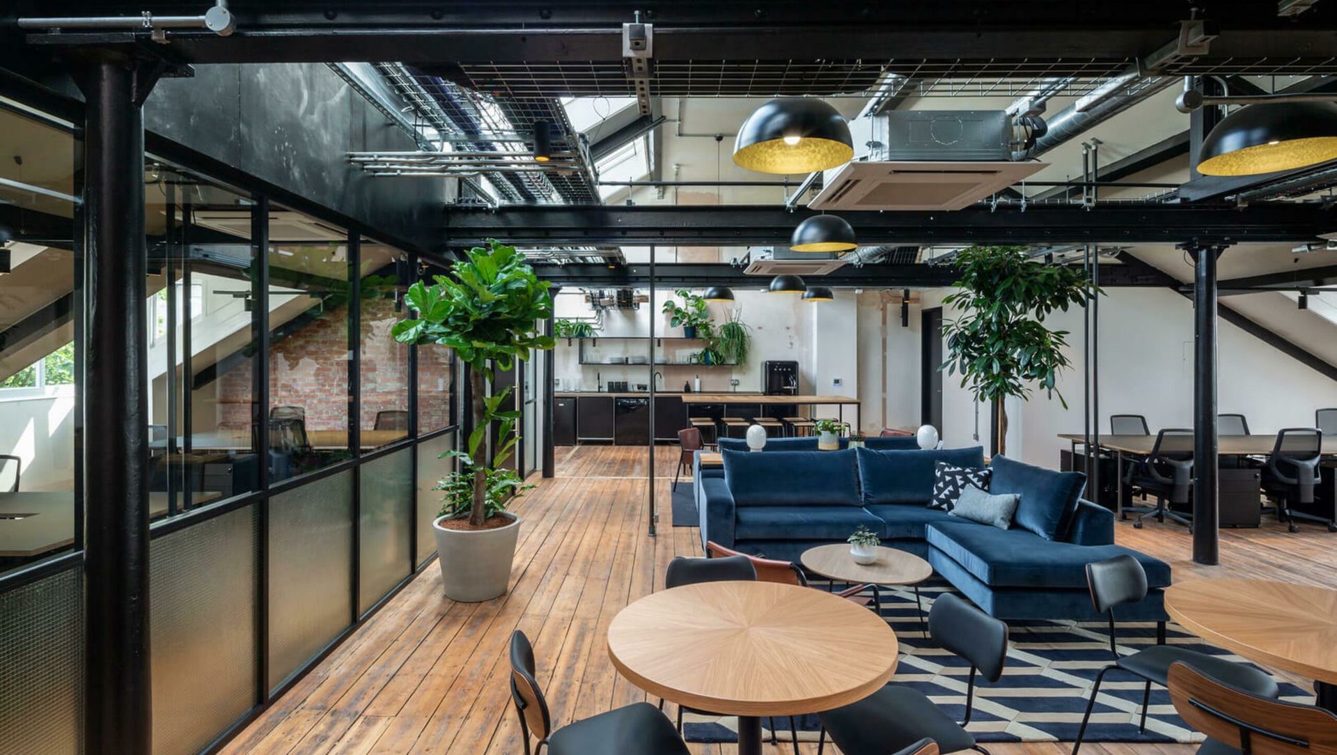 An industrial loft workspace at The Ministry with exposed steelwork, a blue velvet sofa and mature planting